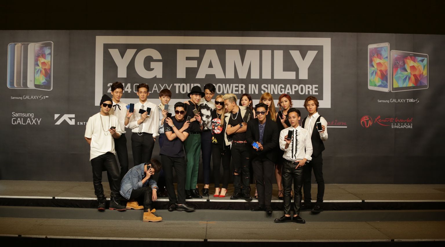 A group photo of the YG Family artistes at the Samsung press conference, posing with the latest Samsung devices